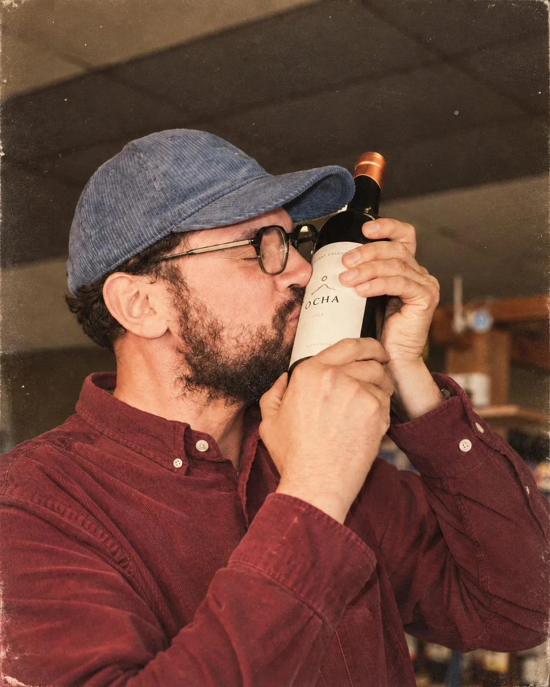 Bertrand, casquette et lunettes, embrasse une bouteille dans la cave