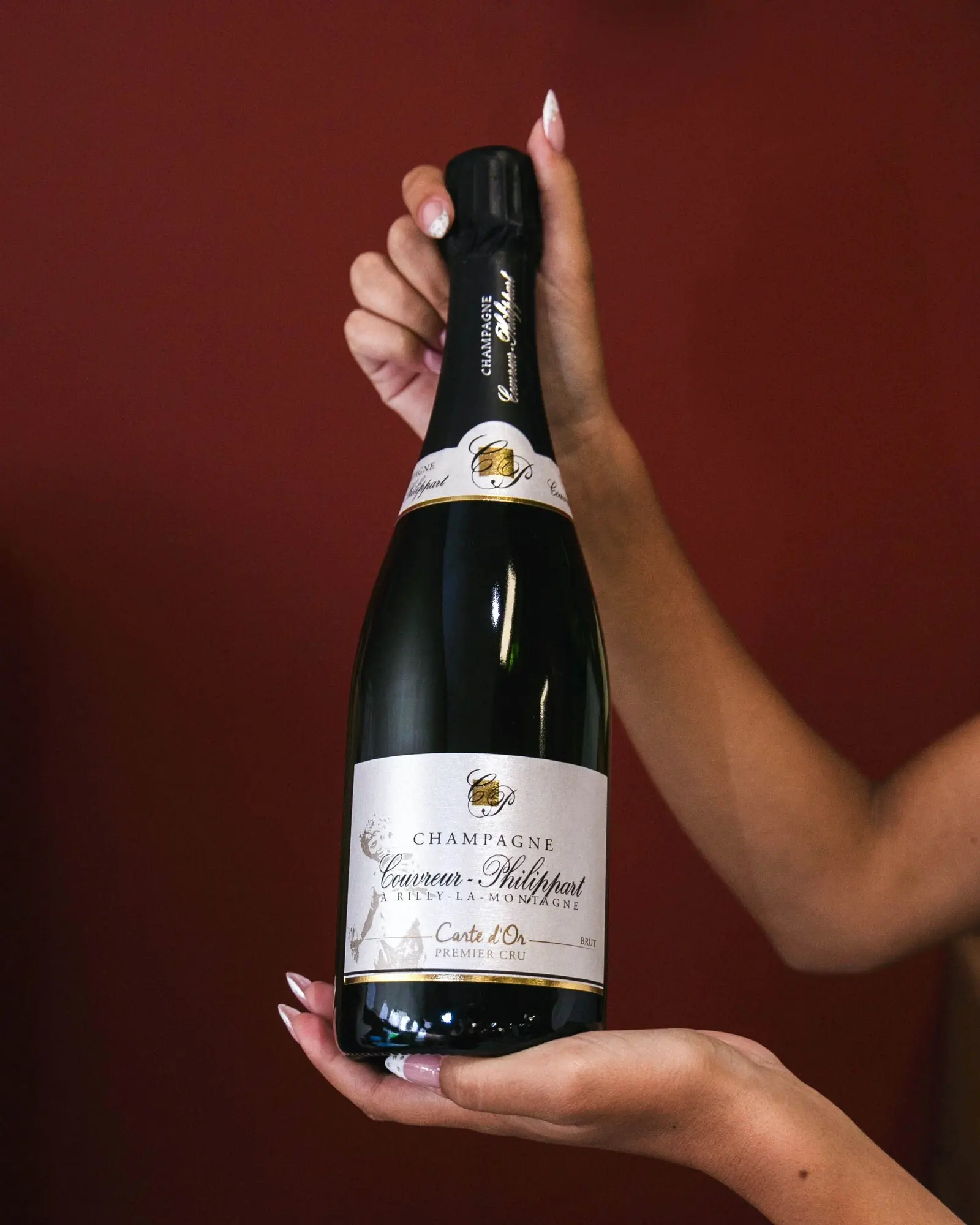 Une bouteille de champagne Couvreur-Philippart Carte d’Or premier cru tenue en main devant un mur rouge.