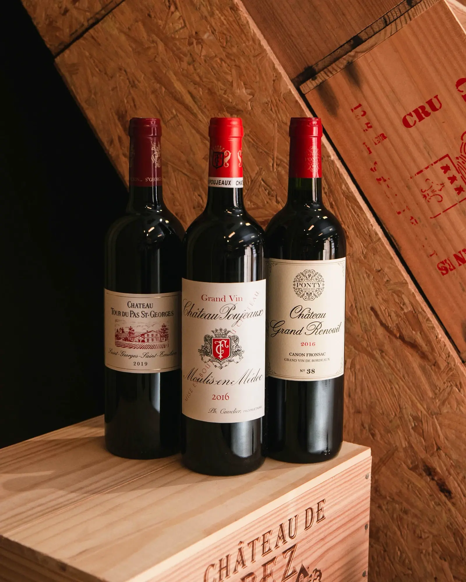 Trois bouteilles de bordeaux rouge posées sur une caisse en bois, dans la cave.
